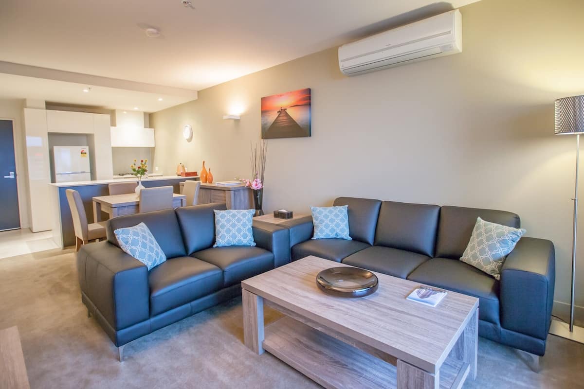 A modern living room with a sectional sofa, a coffee table, and a dining area in the background.