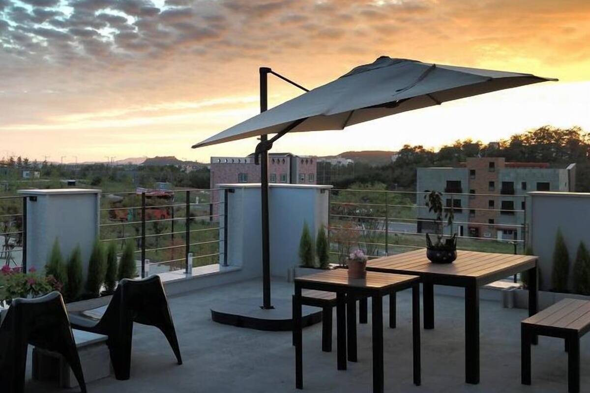 An outdoor patio with a table and chairs, a large umbrella, and a view of buildings and hills in the background.