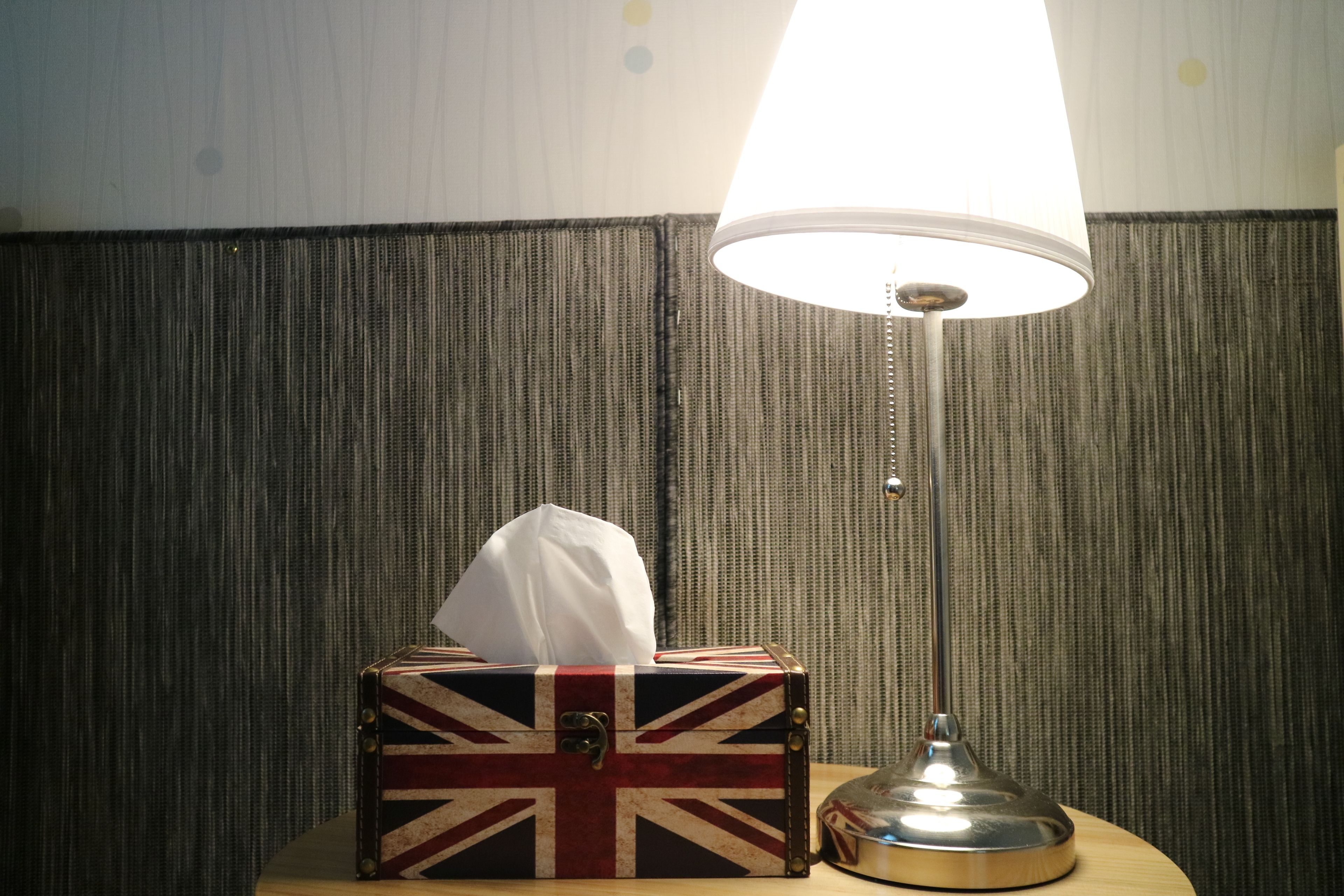 A bedside table with a lamp, a box with a Union Jack design, and a tissue box.