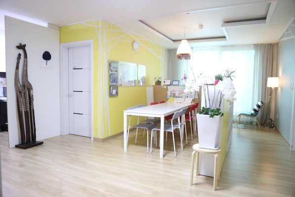 A dining area with a white table and chairs, a yellow accent wall, and a large window with curtains.
