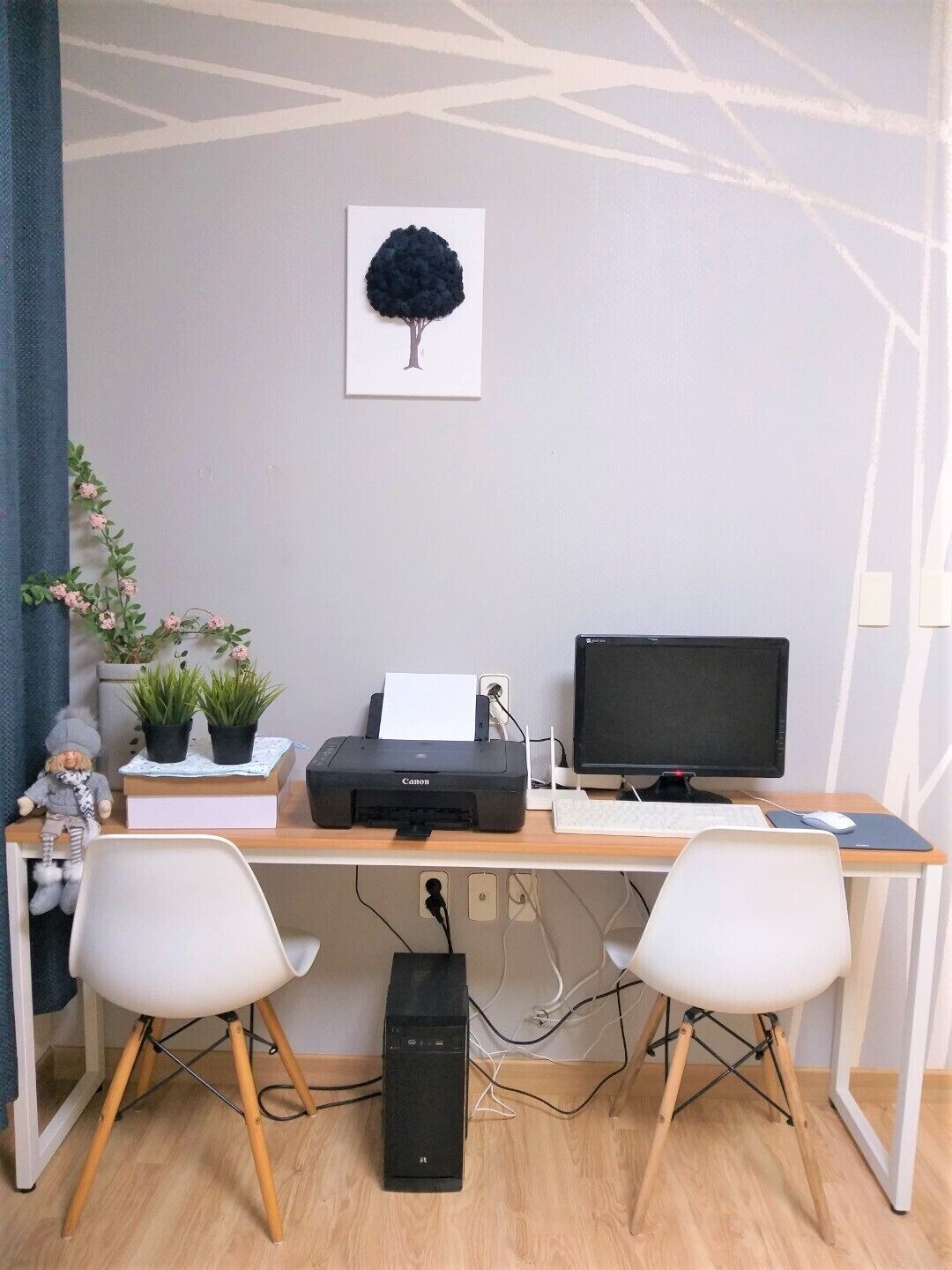 A workspace with a desk, two chairs, a printer, a monitor, and a wall-mounted picture.