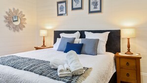 A neatly made bed with a blue and white patterned blanket, two pillows, and a folded towel on a woven rug. There are three framed pictures on the wall above the bed. - Riversleigh Guesthouse (Ballina)