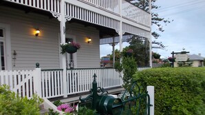 A two-story building with a white exterior, a balcony with hanging flower baskets, and a green mailbox. - Riversleigh Guesthouse (Ballina)
