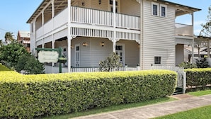 A two-story guesthouse with a balcony, a sign indicating it is a Riversleigh guesthouse, and a well-maintained hedge in front. - Riversleigh Guesthouse (Ballina)