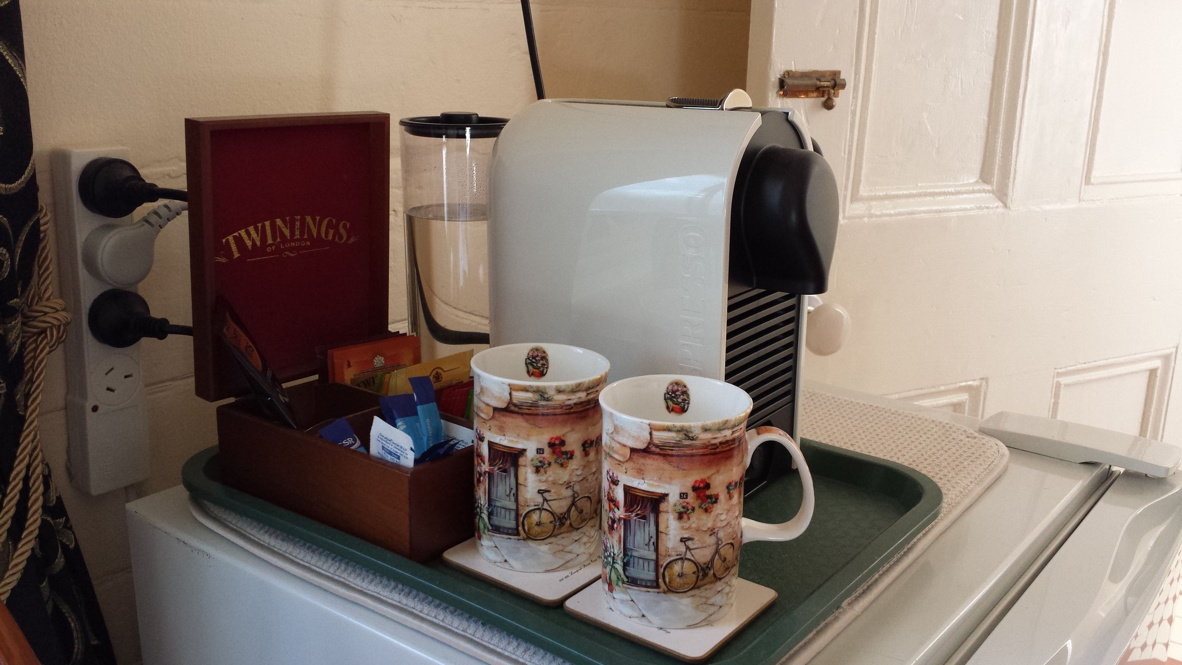 A coffee machine with two cups on a tray, a red box labeled 'TWINSINGS OF LONDON', and a water dispenser.
