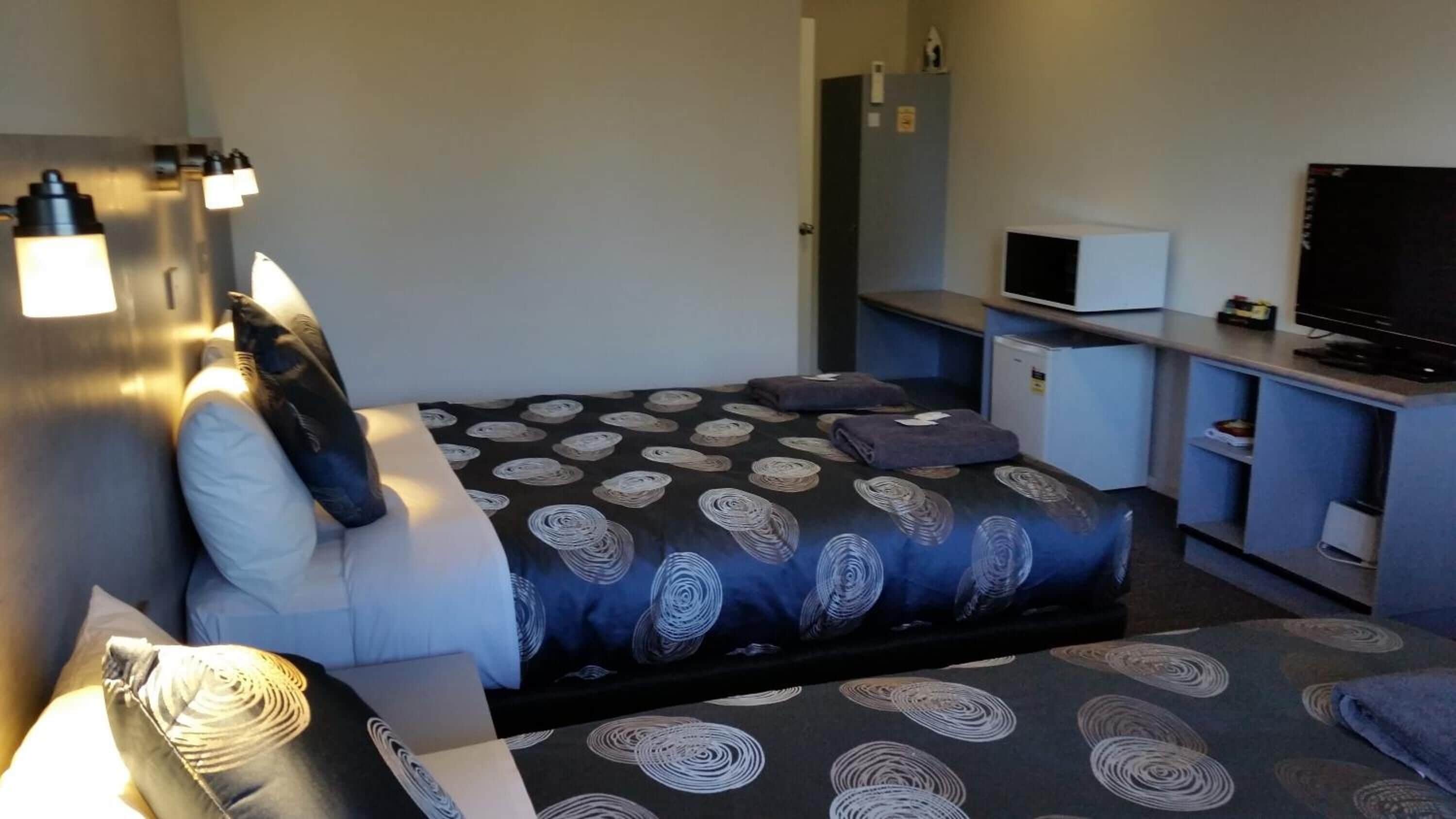 Habitación de hotel con cama, escritorio, televisor y un refrigerador pequeño.