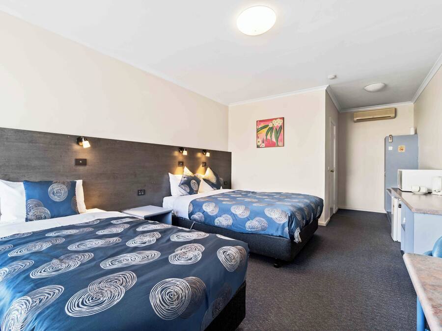 Ein Hotelzimmer mit zwei Betten, einem Schreibtisch, einem Sessel, einem Fernseher und einer Klimaanlage.
