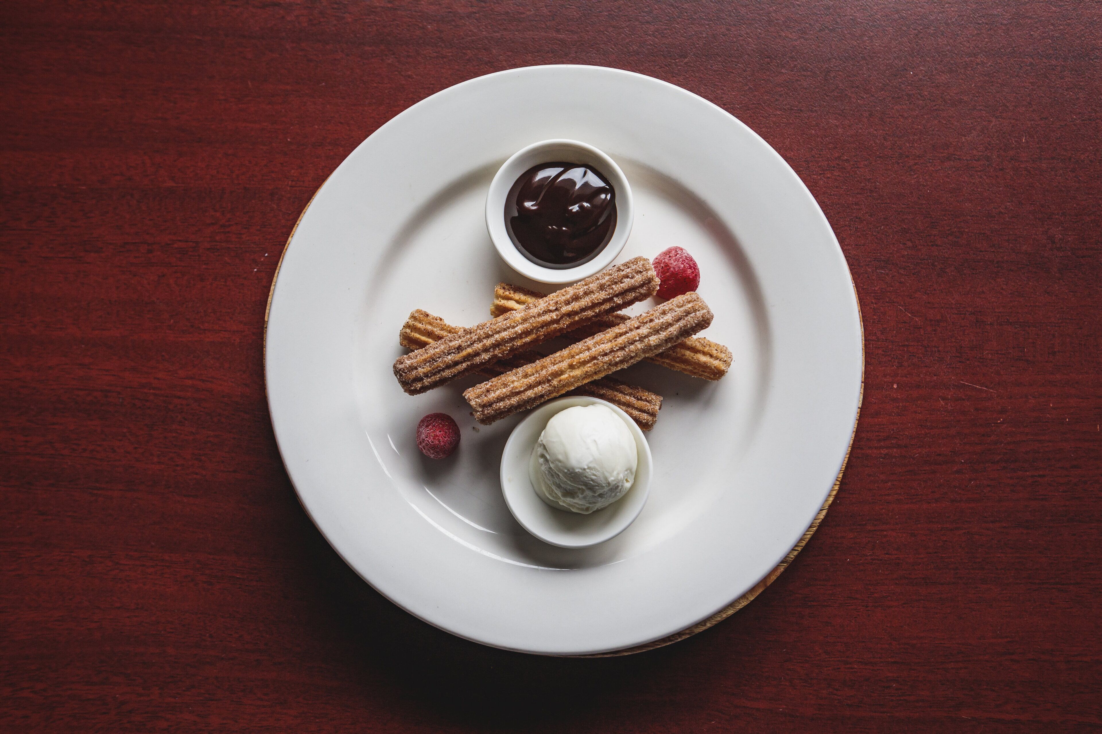 Un plato con churros, salsa de chocolate, una porción de helado y una frambuesa.