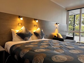 A modern hotel room with a large bed, two bedside tables, and a window with a view of the outdoors.