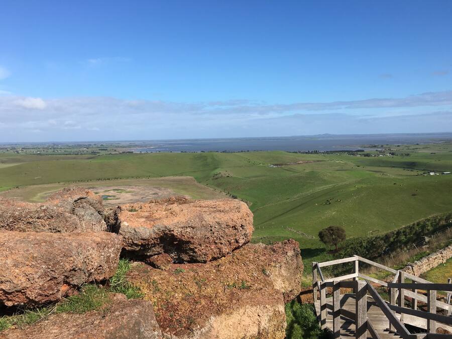 Ein malerischer Ausblick von erhöhter Position auf eine grüne Landschaft, mit einer hölzernen Treppe, die hinabführt.