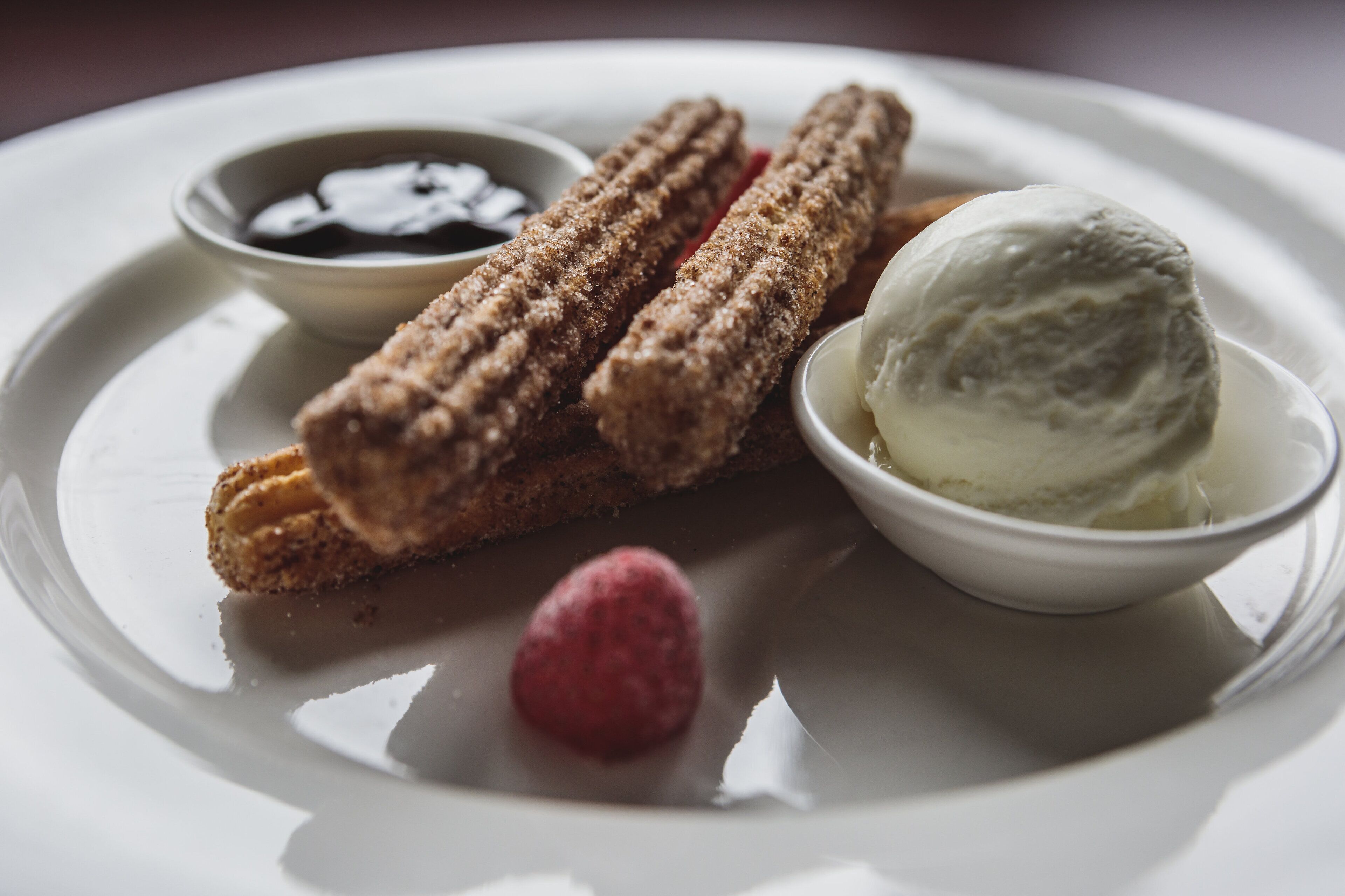 Churros with chocolate dipping sauce, a scoop of vanilla ice cream, and a raspberry on a white plate.