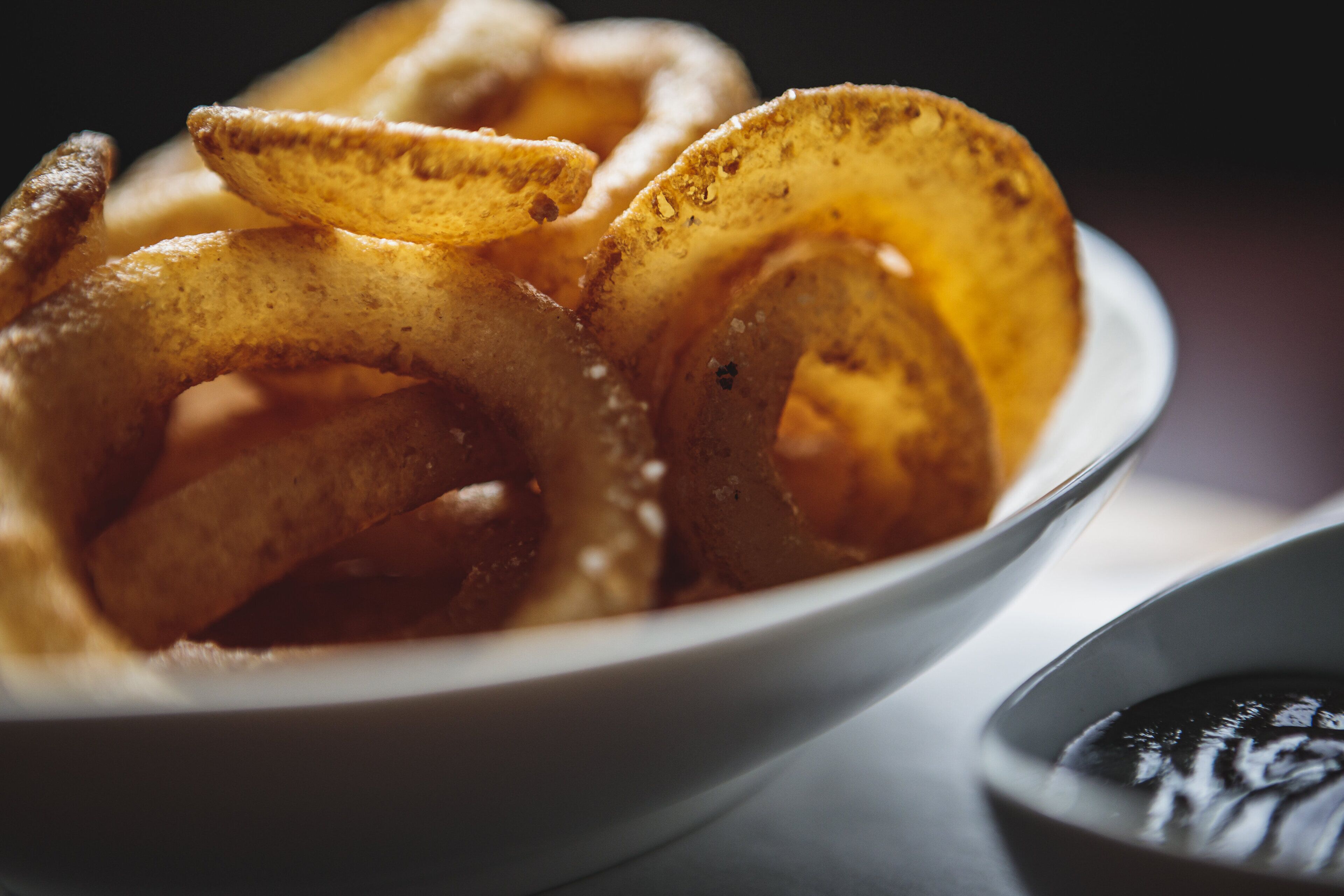 A bowl of onion rings with a side of dipping sauce.