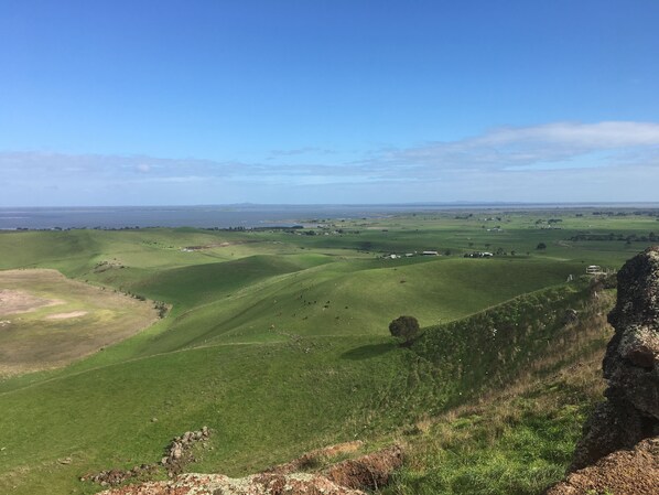 A panoramic view of a green valley with rolling hills and a distant body of water.