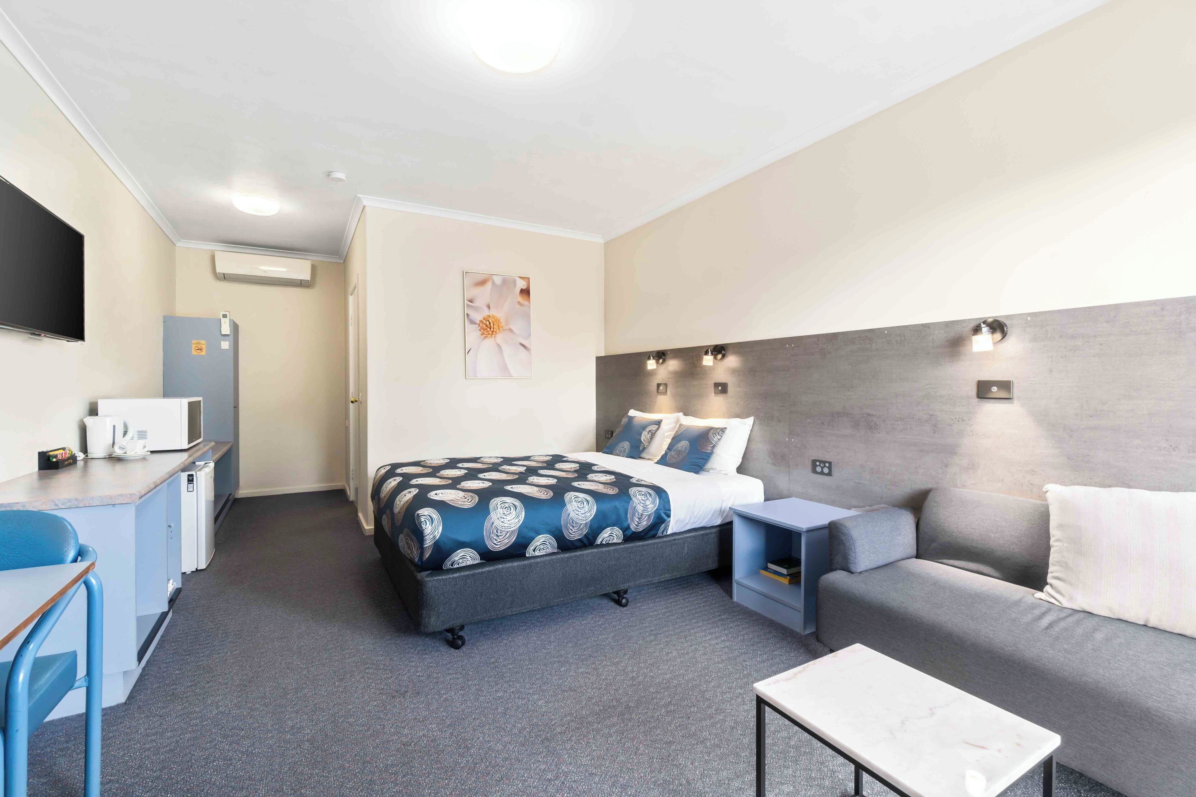 A hotel room with a bed, a desk, a sofa, a small table, and a TV.