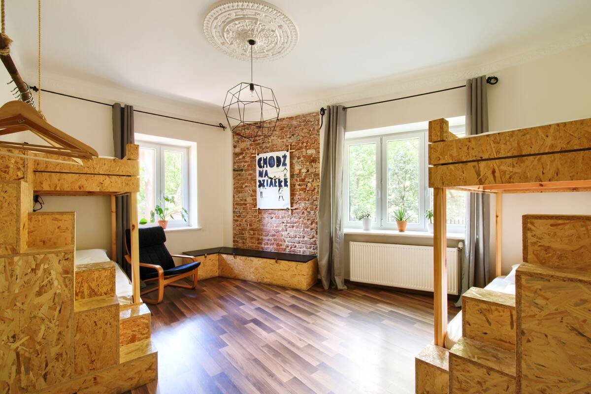A room with a wooden staircase, a hanging light fixture, a brick wall, and a window with a view of greenery.