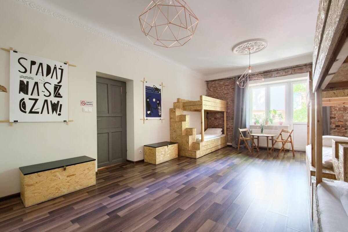 A room with a bunk bed, a desk, and a chair. There is a door and a window.