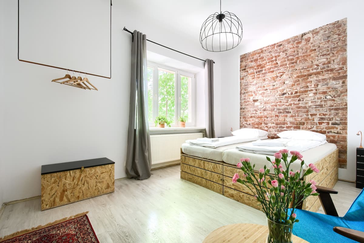 A modern bedroom with a brick wall, a bed with white linens, a hanging light fixture, and a window with curtains.