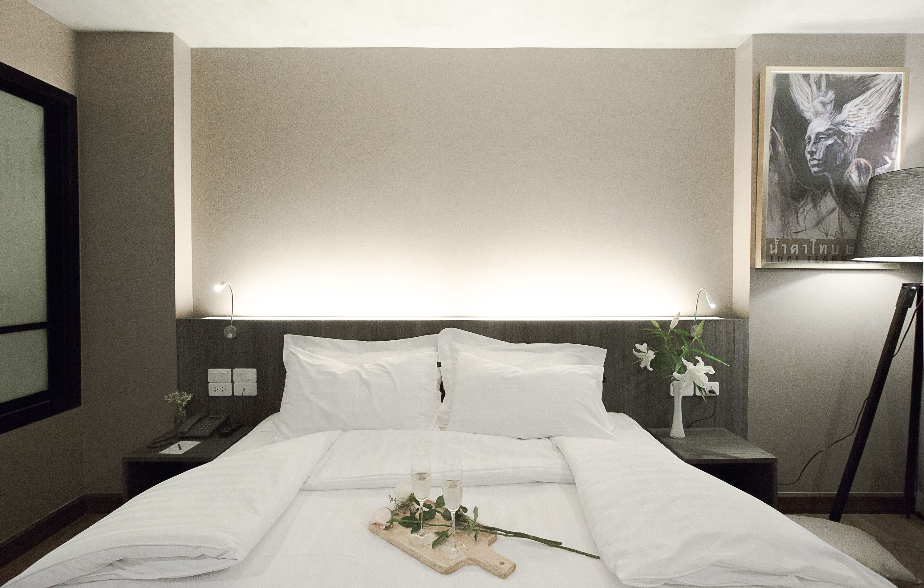 A hotel room with a neatly made bed, bedside lamps, a nightstand with a phone, and a framed picture on the wall.