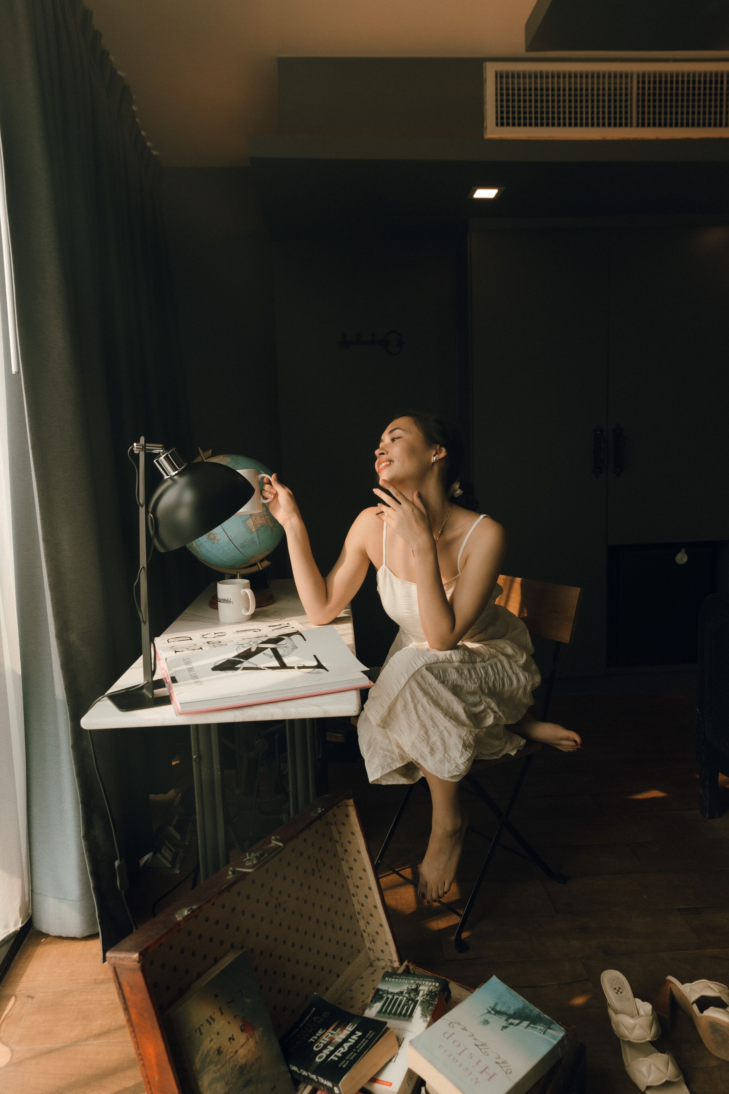 A person seated at a desk with a globe, books, and a lamp.