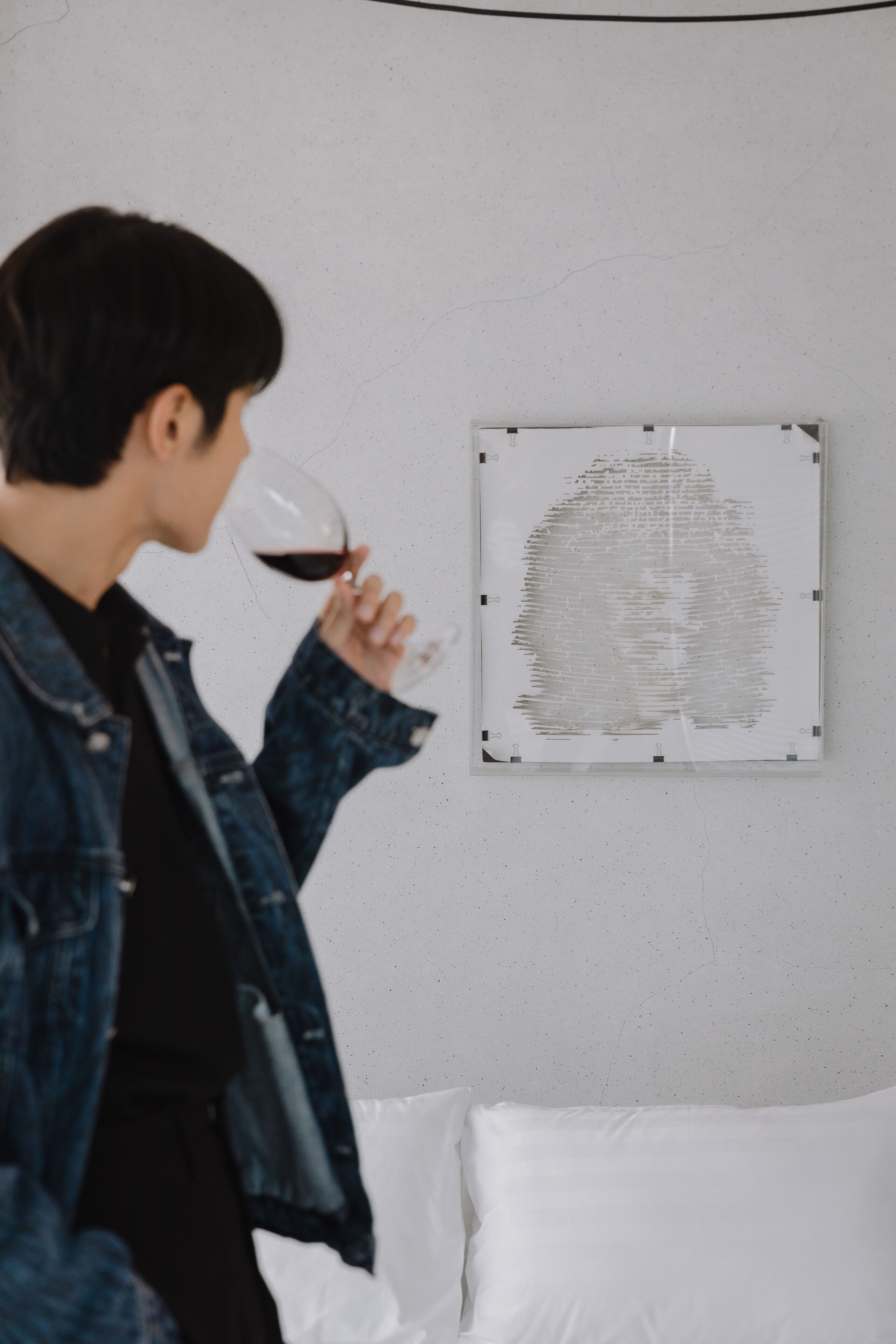 A person holding a wine glass, standing in front of a wall with a framed artwork.