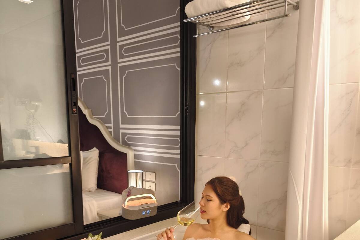 A woman relaxing in a bathtub filled with bubbles and rose petals, with a book and a glass of wine beside her.