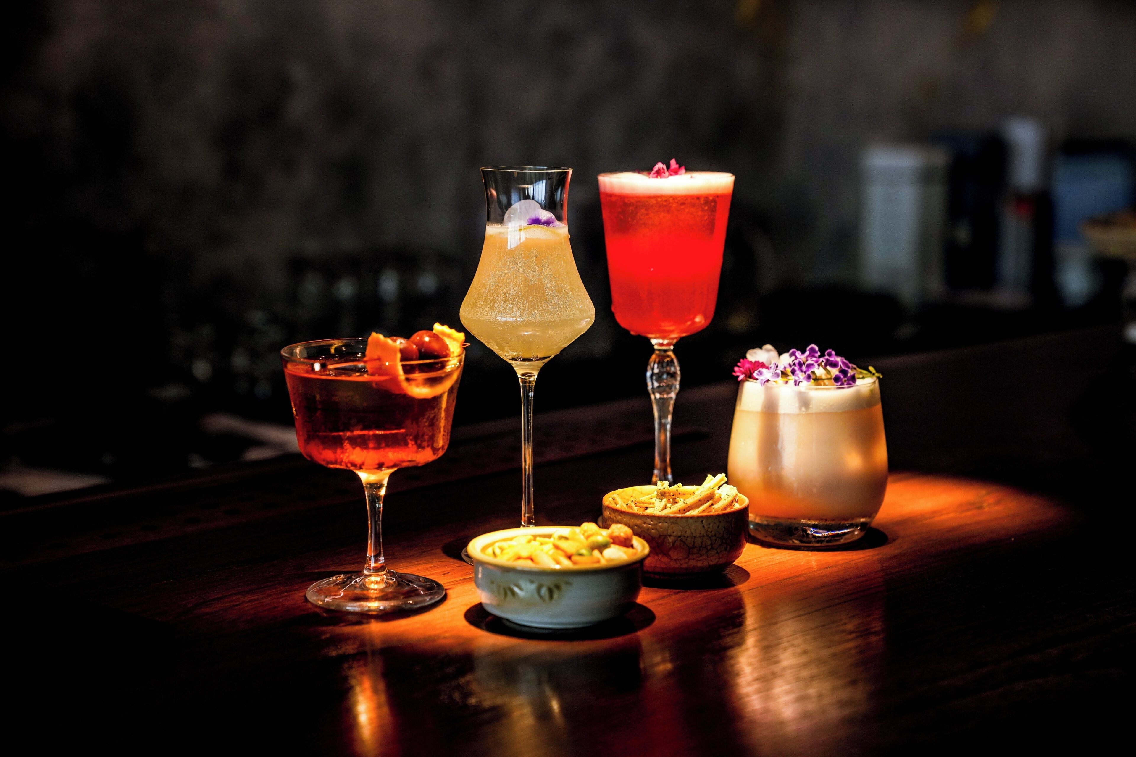 Un bar con cuatro cócteles distintos y un bol de comida.