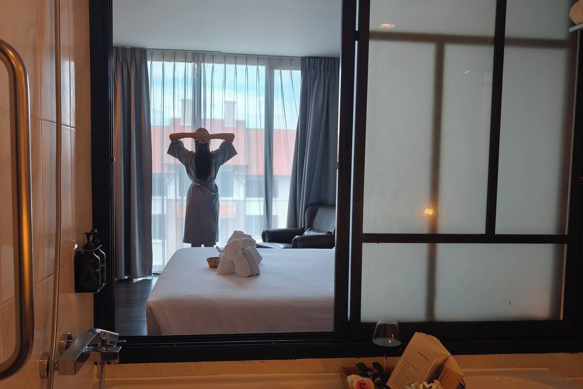 A hotel bathroom with a large bathtub, a shower, and a view of the room through a sliding glass door.