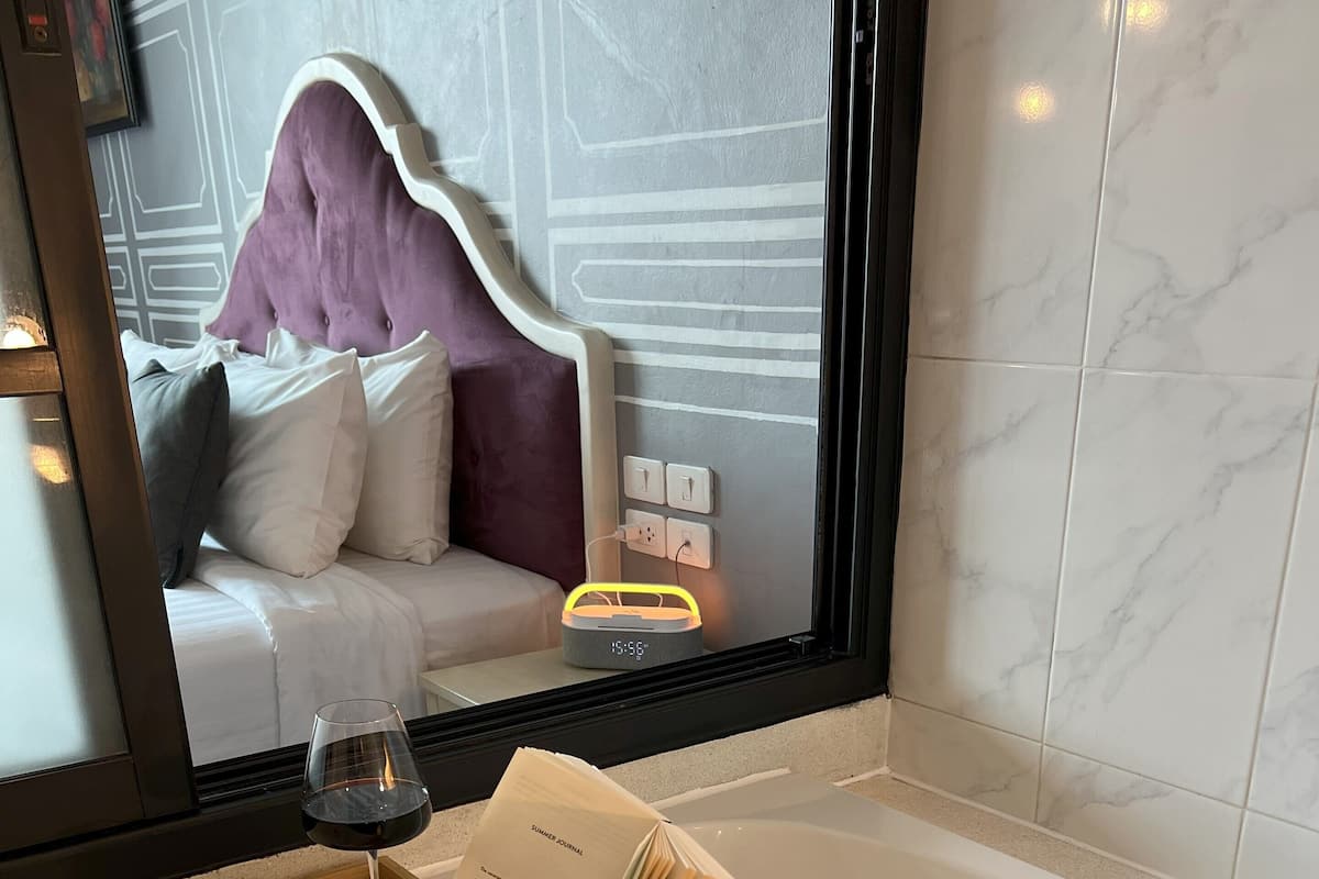 A bathroom with a bathtub, a wooden tray with a candle, rose petals, and a bouquet of flowers.