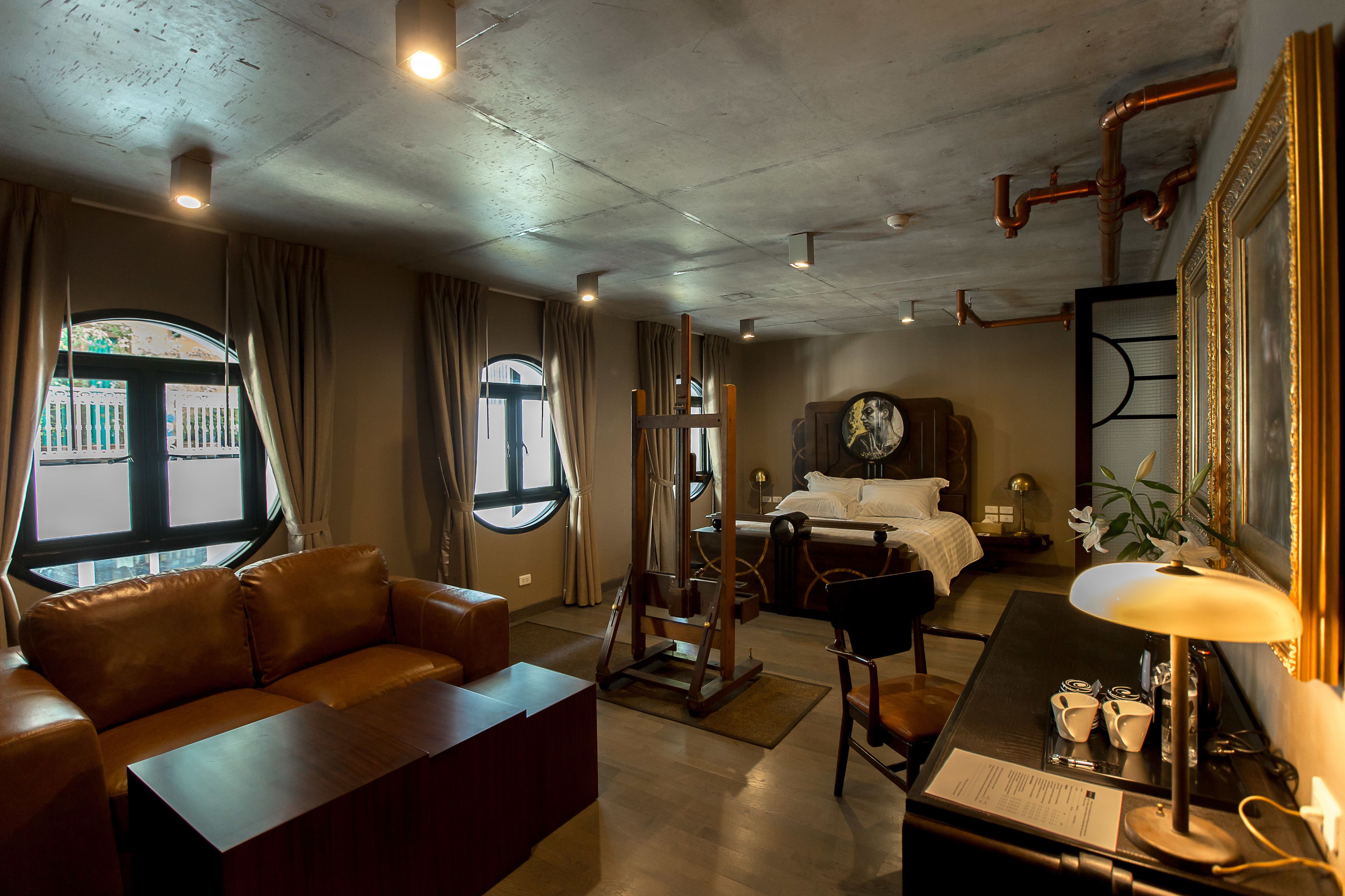 Ein Hotelzimmer mit einer Ledersofa, einem Schreibtisch mit Lampe, einem Bett und einem großen Fenster mit Vorhängen.