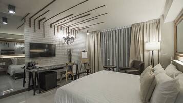 A modern hotel room with a large bed, a desk with a chair, a TV, and a seating area with a chair and a table.
