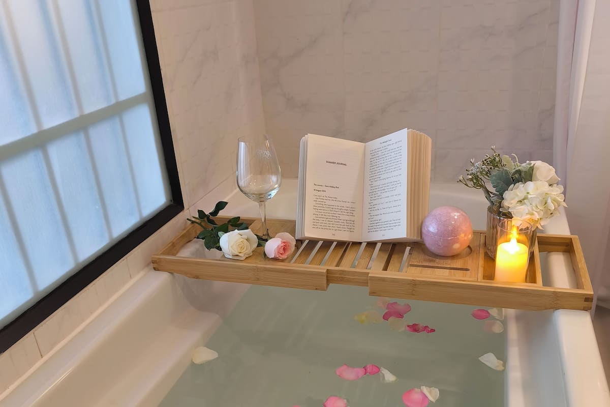 A bathtub with rose petals, a book, a glass of water, and a candle.