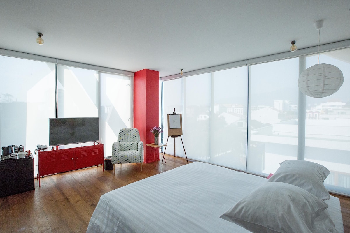 A modern bedroom with a large bed, a red cabinet, a TV, and a desk with a vase.