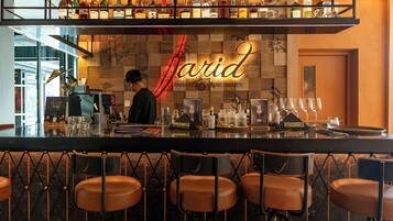 A bar area with a variety of bottles and glasses, a bartender, and several stools.