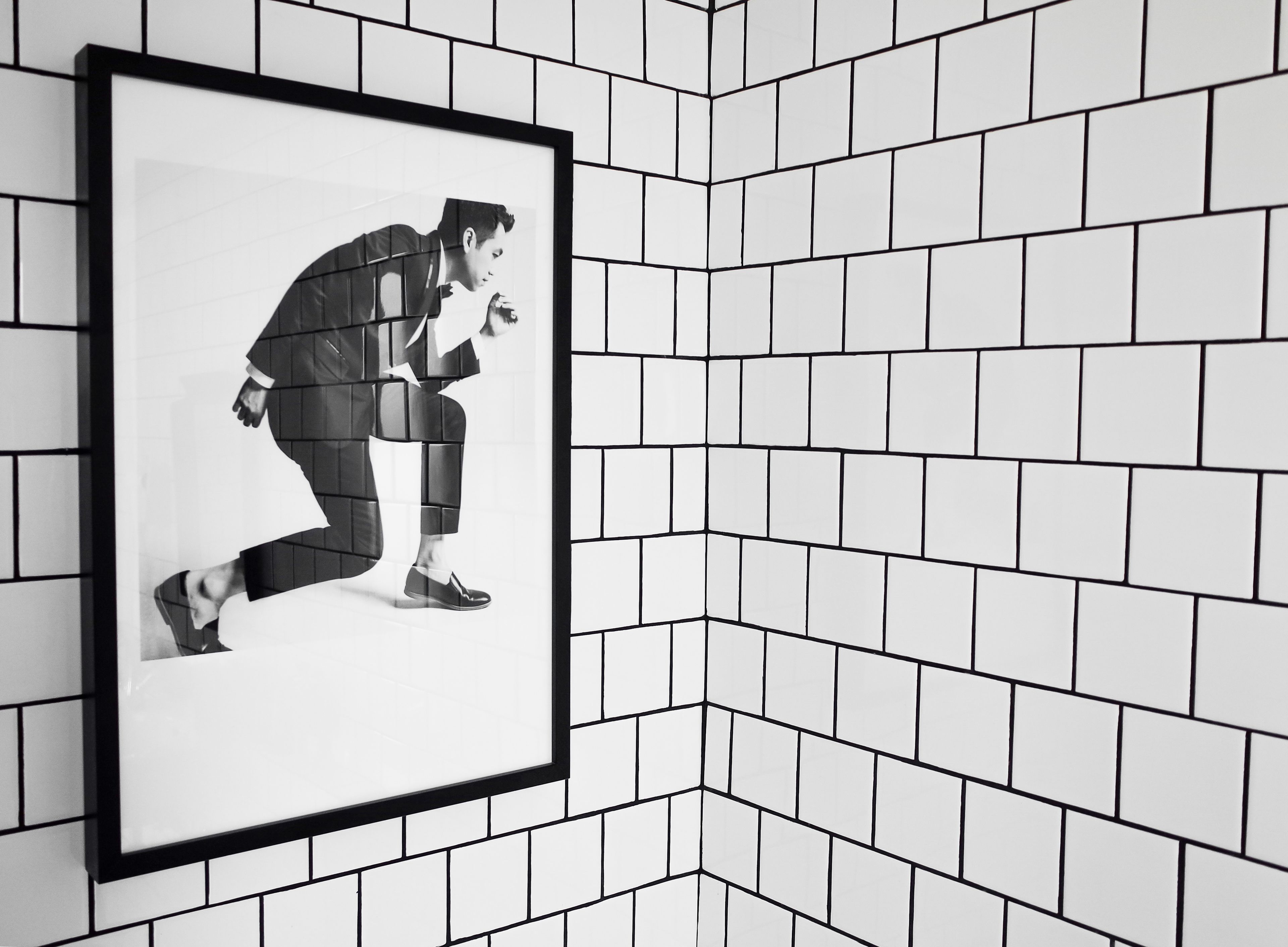 Ein gerahmtes Schwarz-Weiß-Foto einer Person im Anzug an einer gefliesten Wand.