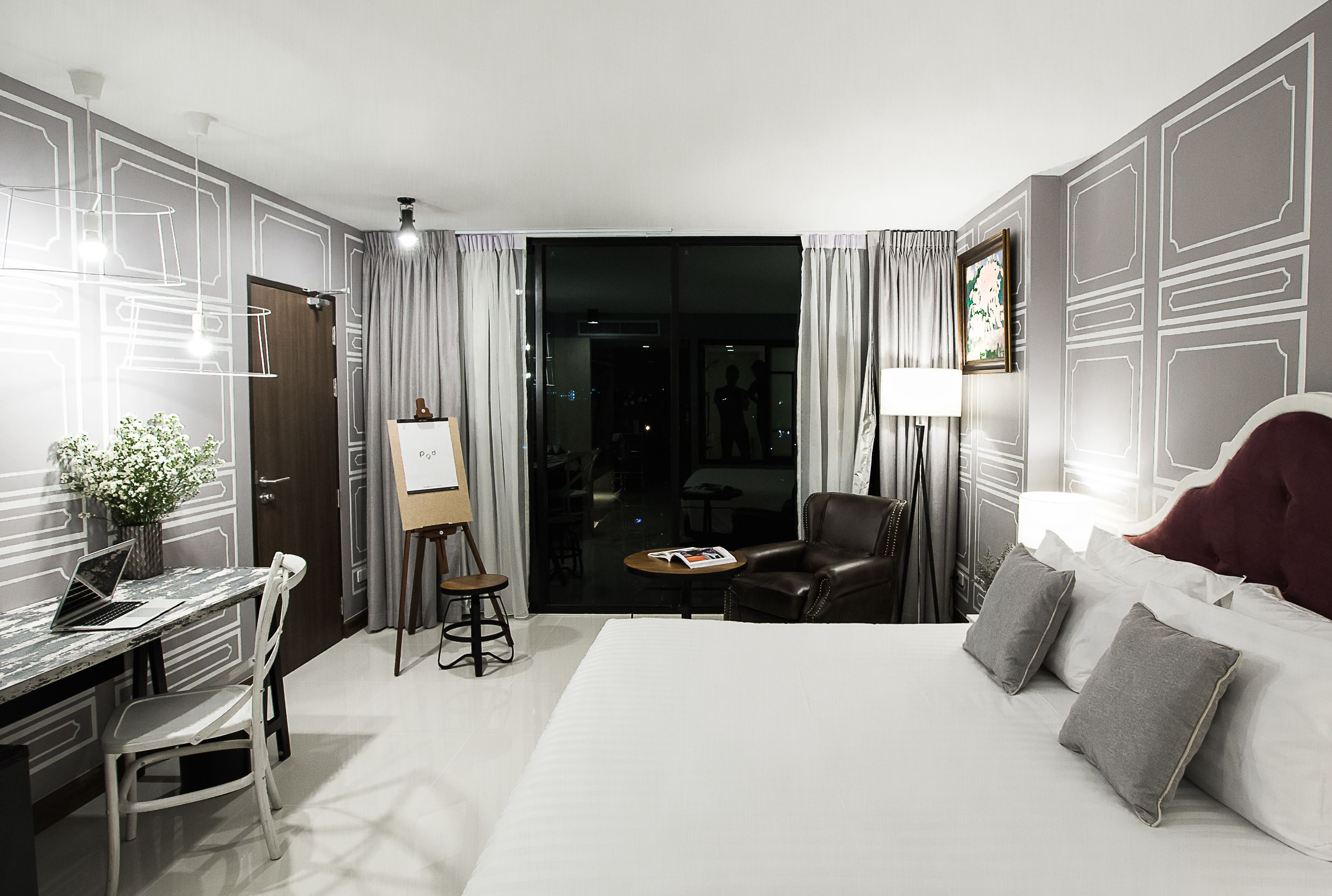 A hotel room with a bed, desk, chair, and a view of the city at night.