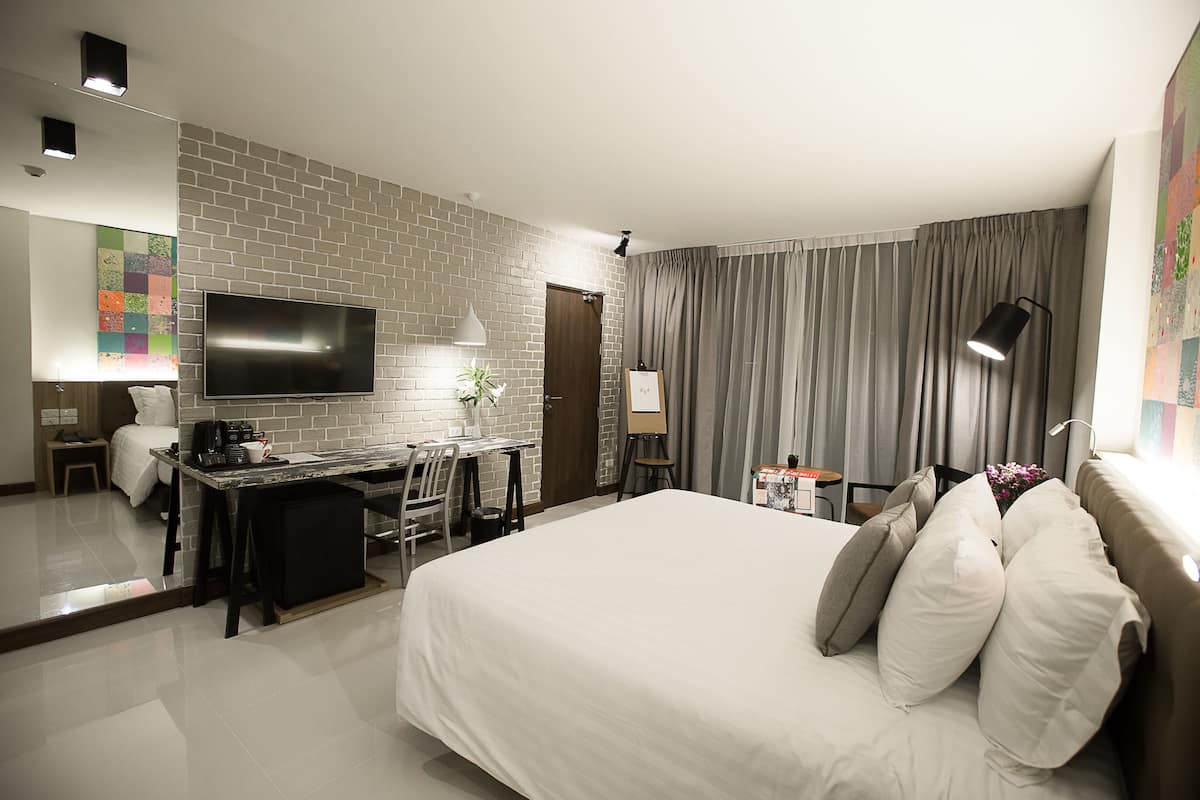 A hotel room with a large bed, a desk with a computer, a flat-screen TV, and a brick accent wall.