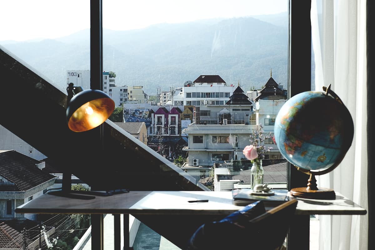 A desk with a globe and lamp, overlooking a cityscape with mountains in the background.