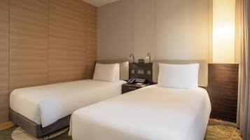 A hotel room with two single beds, a bedside table with a lamp, and a wall-mounted phone.