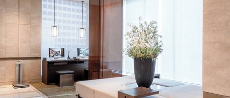 A modern hotel lobby with a reception desk, seating area, and large windows.