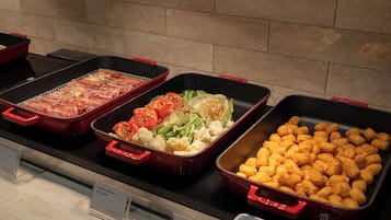 A buffet with various dishes including bacon, vegetables, and tater tots.
