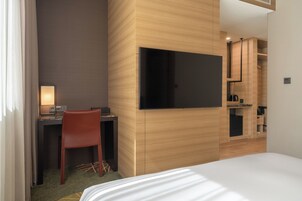 Una habitación de hotel con cama, escritorio con silla, televisor y kitchenette.
