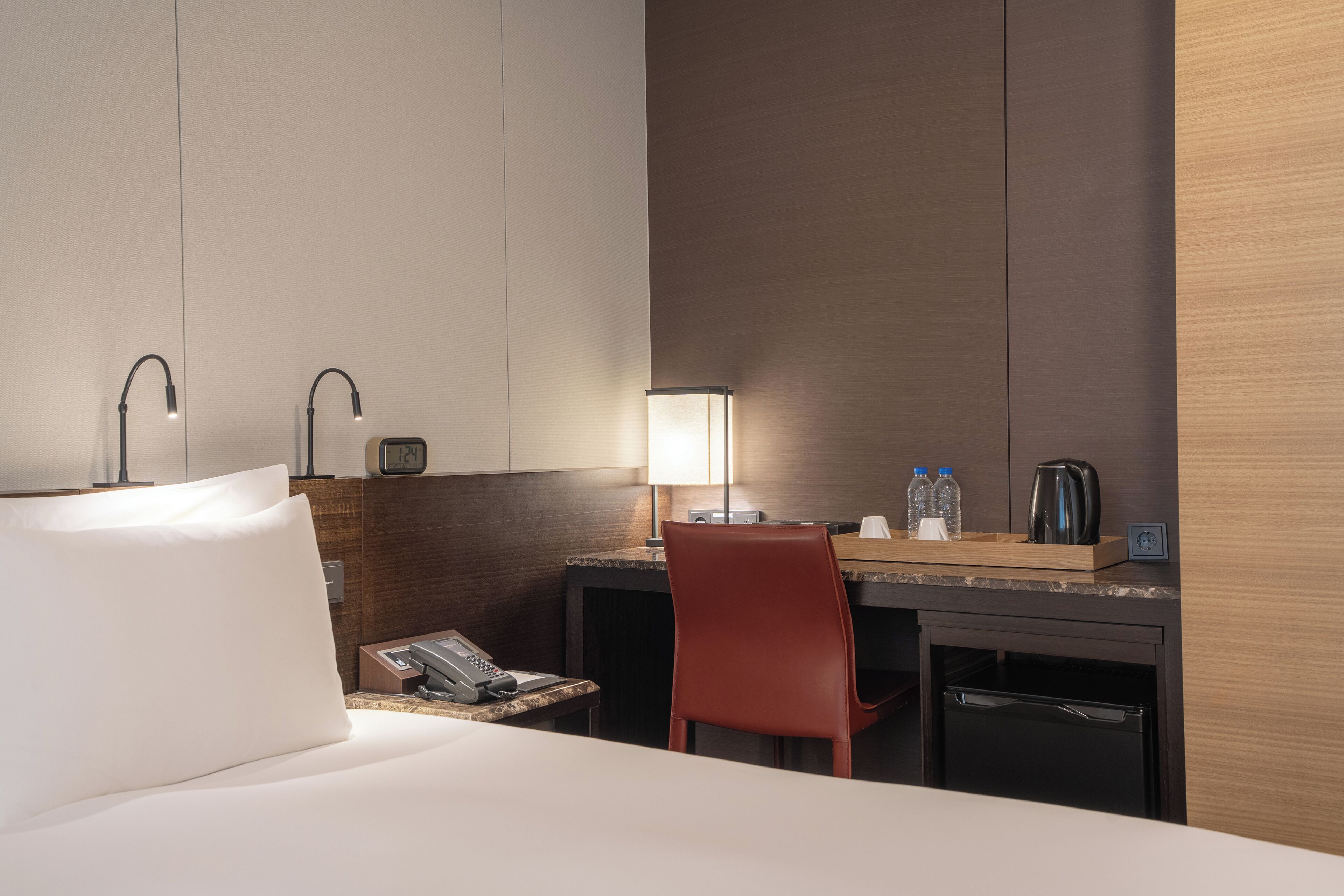 Een hotelkamer met een bed, een bureau, een stoel, een lamp, een telefoon, een koffiezetapparaat en een kleine koelkast.