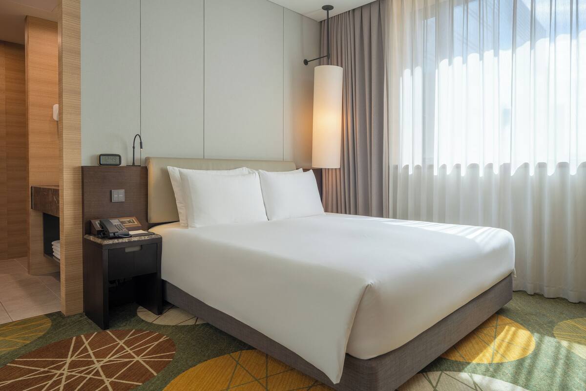A hotel room with a large bed, a bedside table with a phone, and a window with curtains.