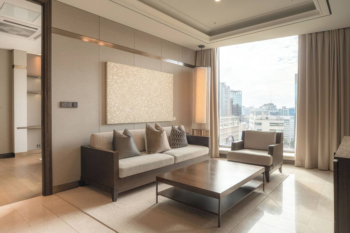 A modern living room with a sofa, a coffee table, and a view of the city through large windows.