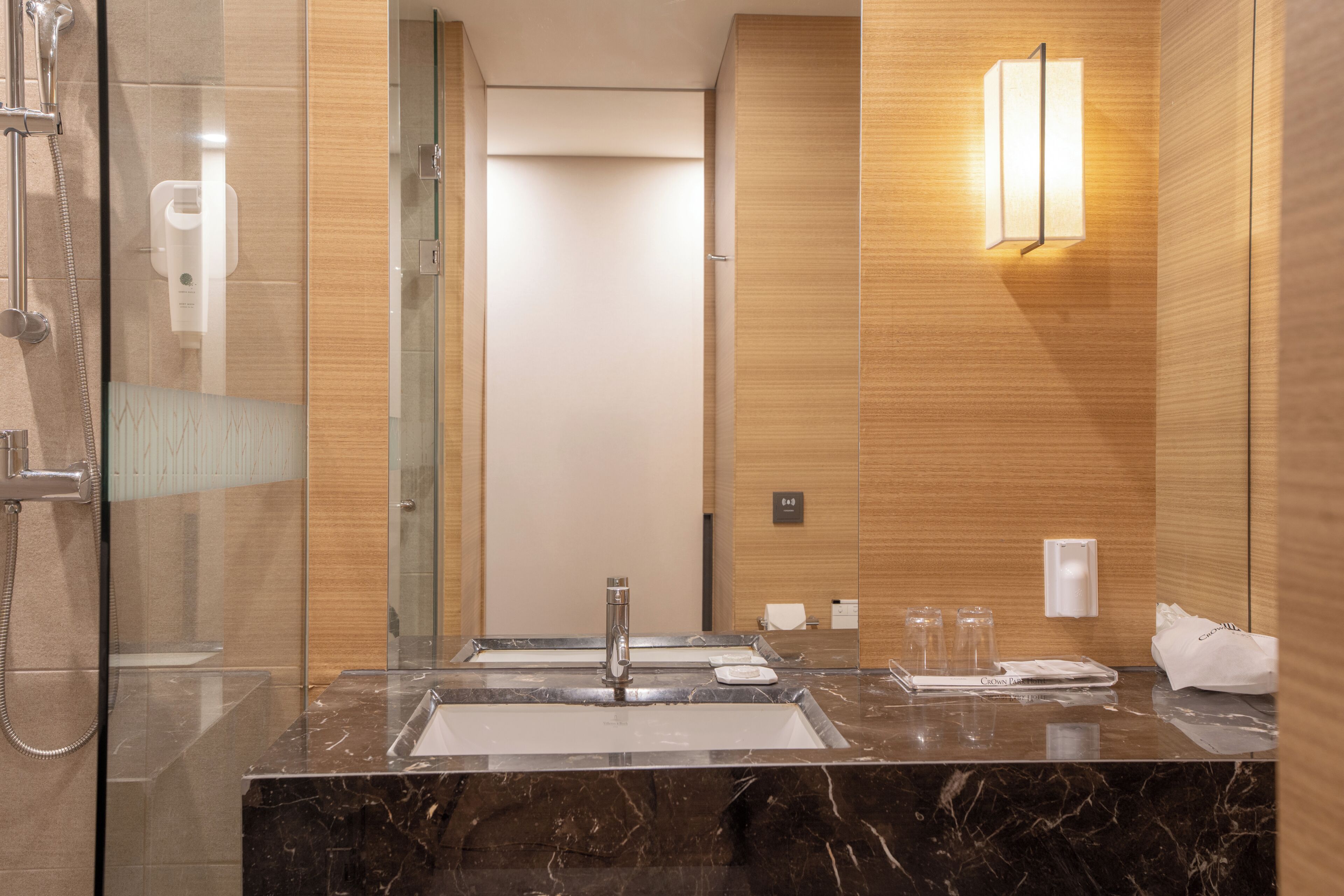 A modern bathroom with a glass-enclosed shower, a sink with a marble countertop, and a wall-mounted light fixture.