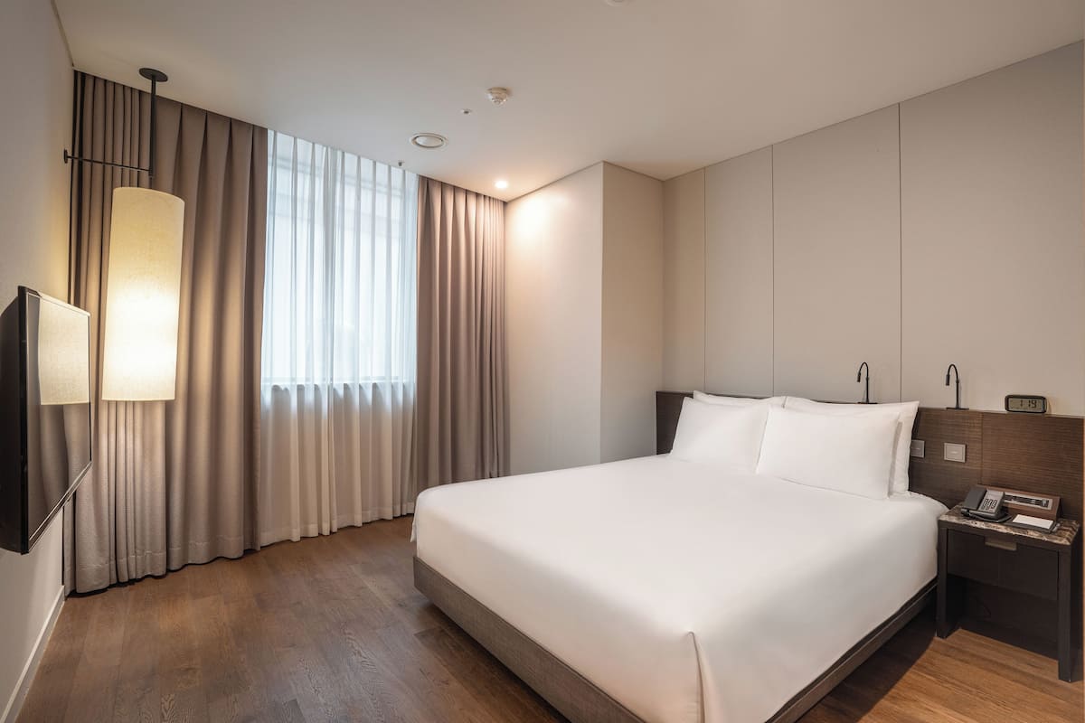 A hotel room with a large bed, a bedside table with a phone, and a wall-mounted TV.