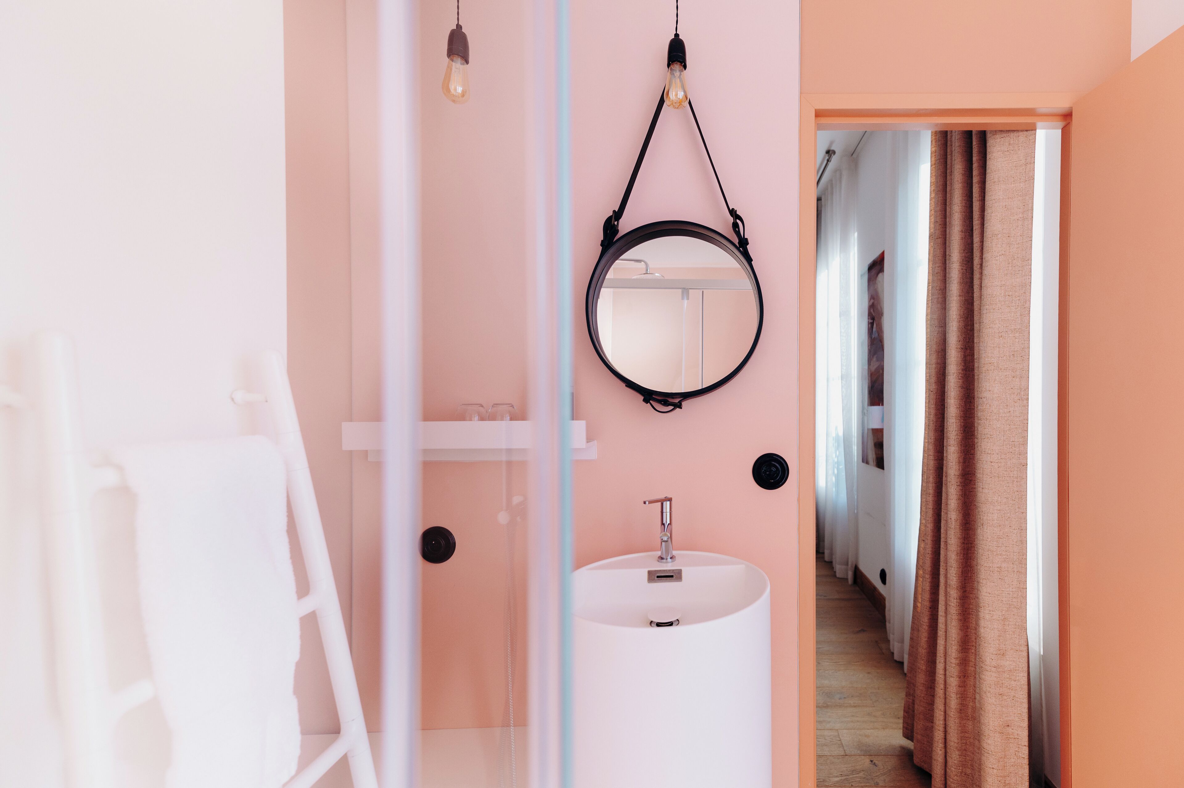 A bathroom with a white sink, a round mirror, and a light bulb hanging from the ceiling.