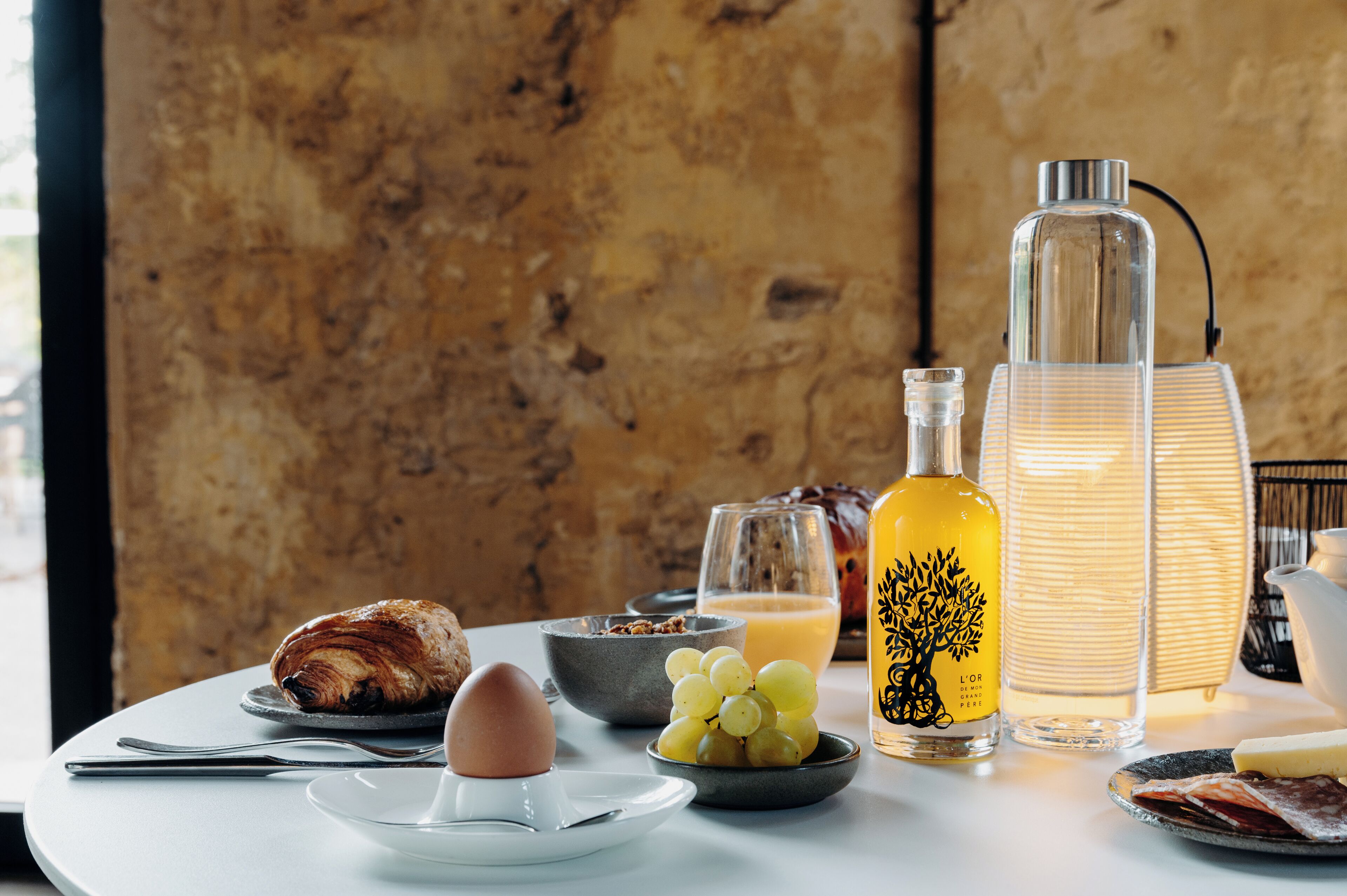 Ein Frühstückstisch mit Croissants, Eiern, Trauben, Saft und einer Flasche L'Oréal Paris Parfüm.