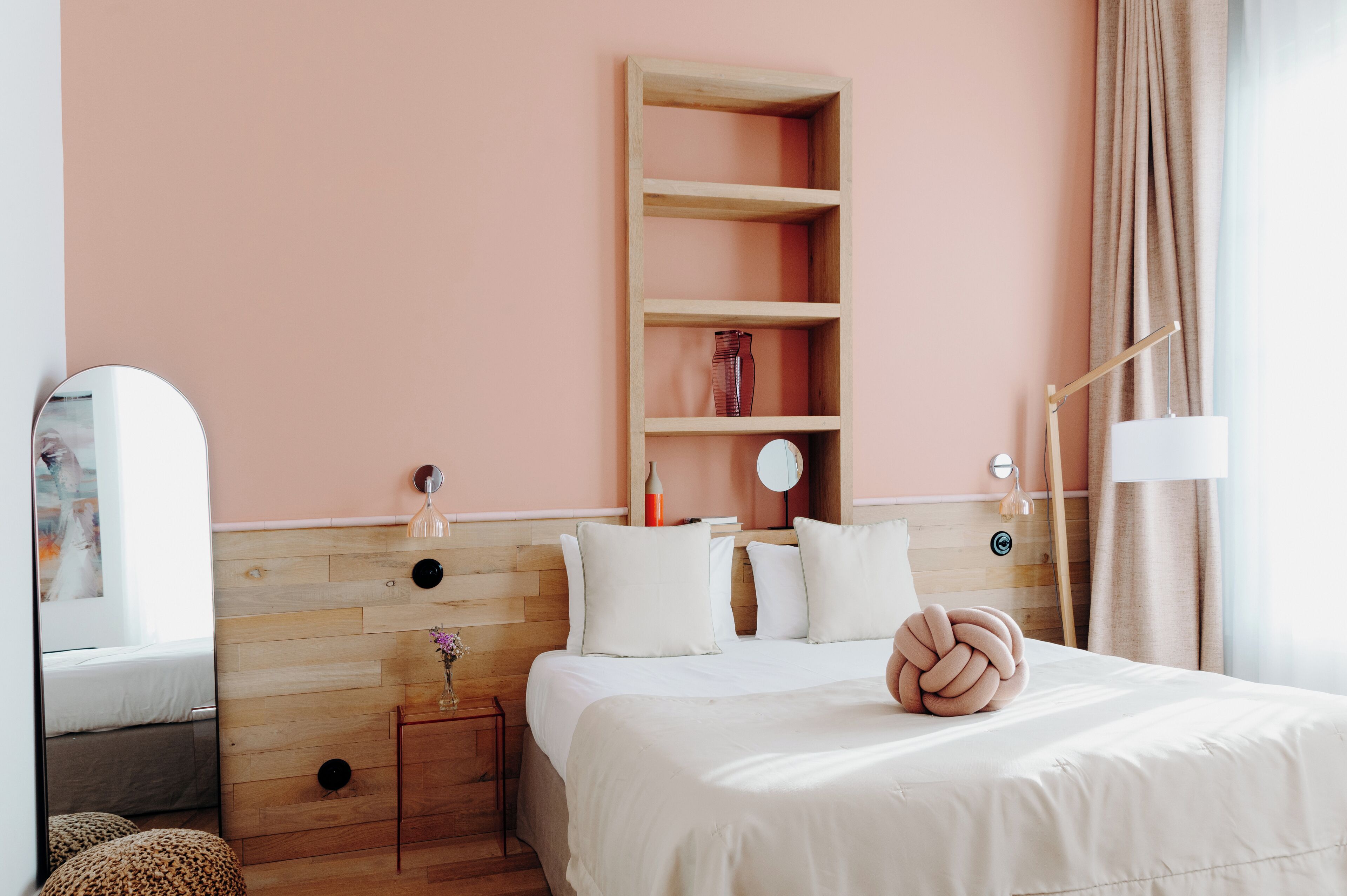 A bedroom with a wooden headboard, a bedside table with a vase, a mirror, and a bed with white bedding.