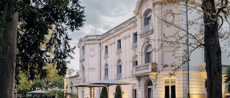 Un edificio imponente de arquitectura clásica, con un amplio patio con asientos al aire libre y un jardín bien cuidado.